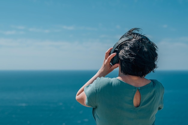 Retrato de mulher adulta ouve música em fones de ouvido, montanhas de verão desfrutam de pensionista