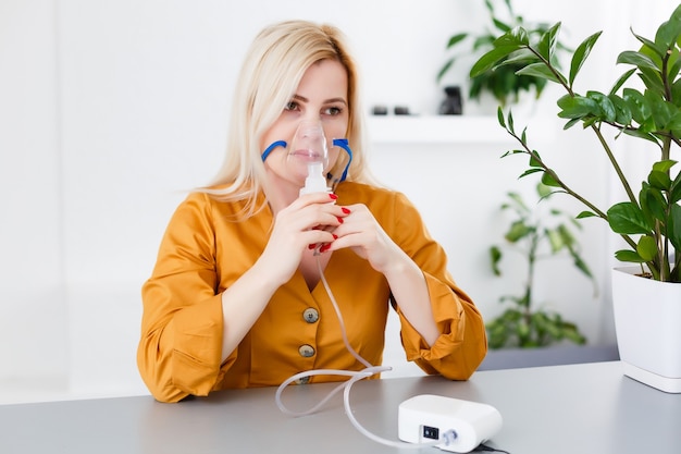 Retrato de mulher adulta usando nebulizador de vapor de vapor fazendo tratamento de medicamento para inalação de aerossol em casa ou em hospital, cura do vírus da gripe e bronquite asmática