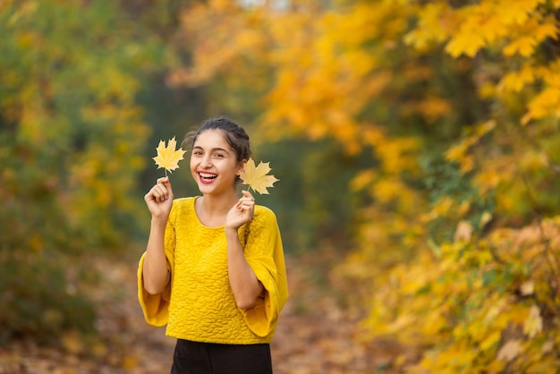 Retrato de mulher alegre com folhas de bordo de outono no parque