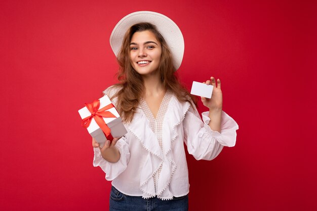 Retrato de mulher alegre e elegante em trajes formais segurando uma caixa de presente e um cartão de crédito