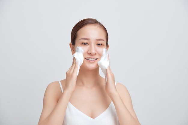 Retrato de mulher alegre rindo, aplicando espuma para lavar o rosto.