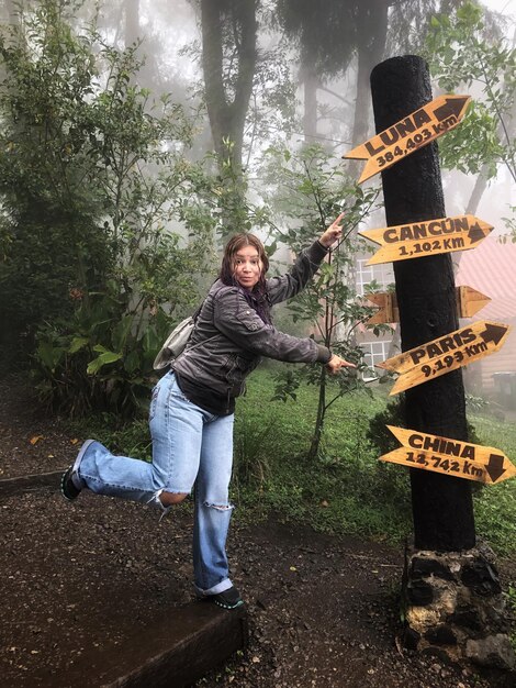 Foto retrato de mulher apontando para um sinal de informação na floresta