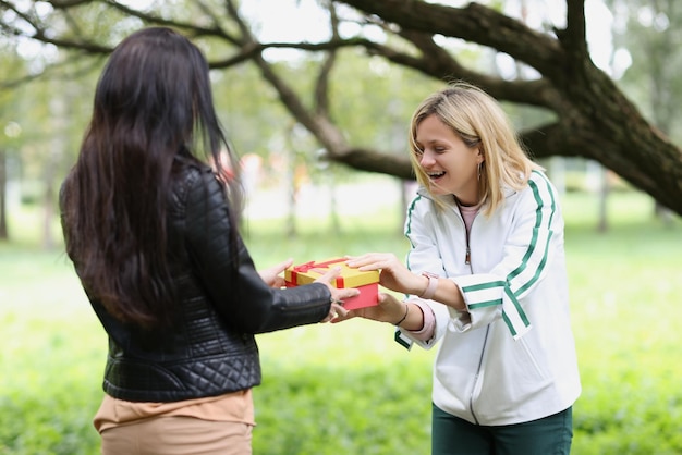 Retrato de mulher apresentando presente para amigo no parque feminino dando caixa de presente para amigo surpreso