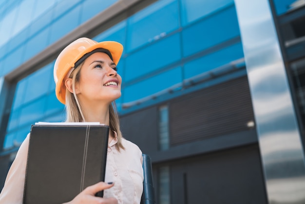 Retrato de mulher arquiteto profissional usando capacete amarelo e olhando para o exterior de um edifício moderno. Conceito de engenheiro e arquiteto.