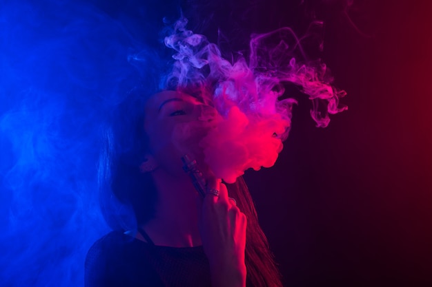 Retrato de mulher asiática fumando vapor ou ecigarette em luz de néon em fundo preto.
