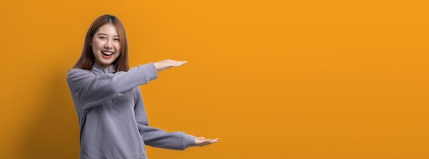 Retrato de mulher asiática gesticulando apontando para o espaço vazio para o conceito de retrato de texto de anúncio usado para propaganda e sinalização isolada sobre o espaço de cópia de fundo amarelo