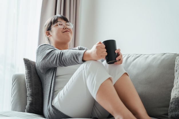 Retrato de mulher asiática relaxando em casa com uma xícara de café ou chá sentado no sofá na sala de estar