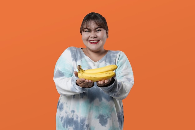 Retrato de mulher asiática segurando banana, isolada em fundo laranja, conceito de nutrição saudável