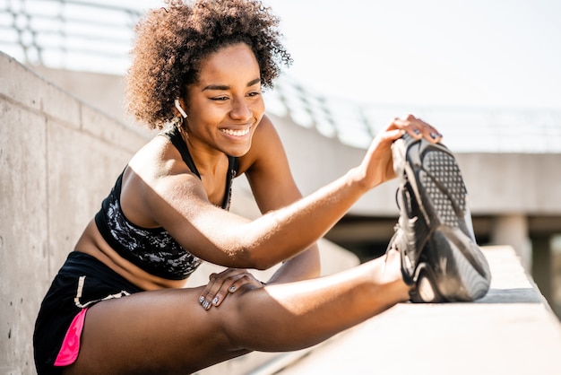 Retrato de mulher atleta afro esticando as pernas antes de fazer exercícios ao ar livre
