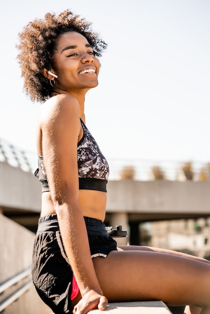 Retrato de mulher atleta afro relaxando e sentada depois do treino ao ar livre