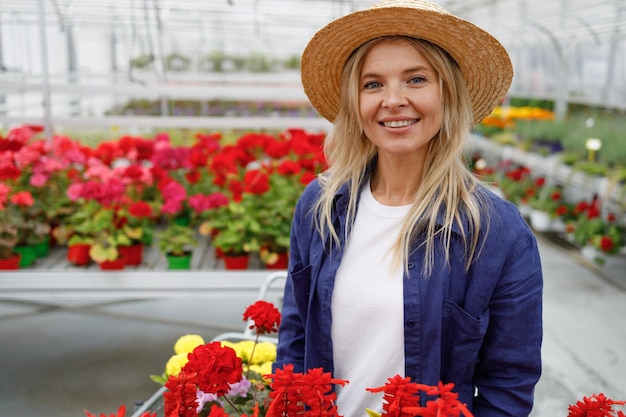 Retrato de mulher atraente em uma camisa e chapéu de palha em uma estufa com flores