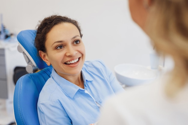 Retrato de mulher atraente na cadeira odontológica conversando com médico dentista