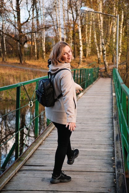 Retrato de mulher atraente vai e brinca na ponte sobre o rio no parque outono