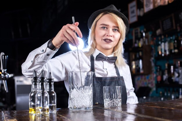 Retrato de mulher bartender adiciona ingredientes a um coquetel enquanto está perto do balcão do bar no pub