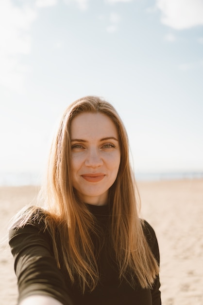 Retrato de mulher bonita com cabelo comprido, loira tira selfie no celular na praia de areia