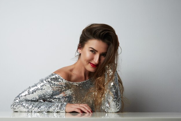 Foto retrato de mulher bonita jovem alegre com vestido prata e posando no estúdio branco vazio.