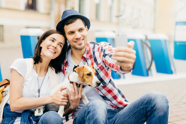 Retrato de mulher bonita jovem alegre, inclinando-se para o marido bonito, sorrindo alegremente para a câmera enquanto posava para selfie.