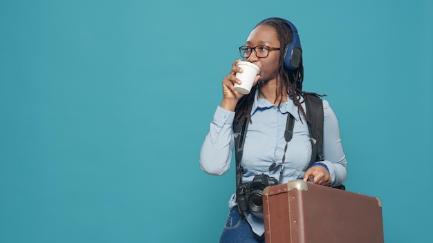Retrato de mulher carregando mala e mochila para fazer uma viagem de férias, tirando fotos com a câmera. fotógrafo com fones de ouvido tomando café e viajando com equipamento fotográfico.