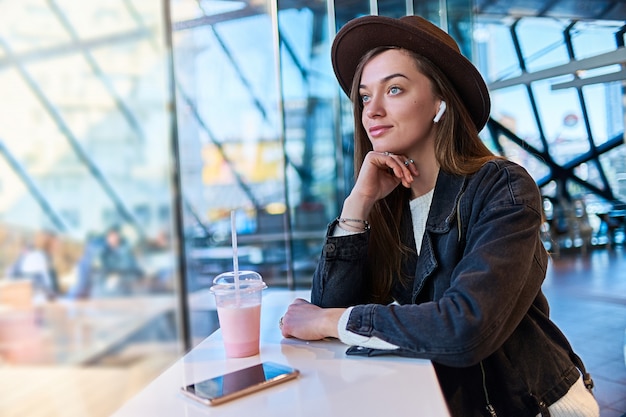 Retrato de mulher casual na moda hipster atraente elegante no chapéu com fones de ouvido sem fio no café. pessoas modernas com estilo de vida digital de tecnologia