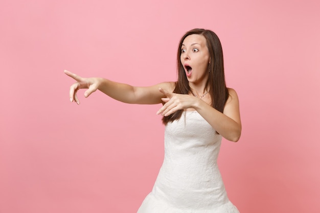 Retrato de mulher chocada com a boca aberta em um vestido branco em pé, apontando o dedo indicador para o lado