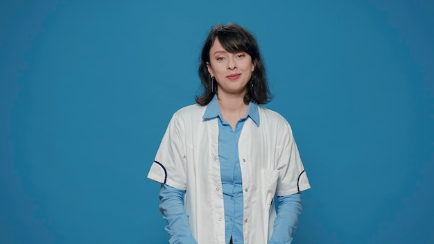 Retrato de mulher cientista cruzando os braços sobre fundo azul, vestindo jaleco branco de laboratório. pesquisador de química se preparando para trabalhar em experimentos científicos e descoberta de microbiologia.