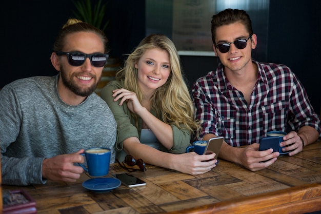 Retrato de mulher com amigos do sexo masculino usando óculos escuros em uma cafeteria