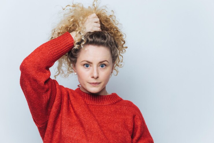 Foto retrato de mulher com cabelo encaracolado parece com expressão confiante e séria para a câmera vestida de suéter vermelho isolado sobre fundo branco lindas poses femininas sozinhas contra fundo branco