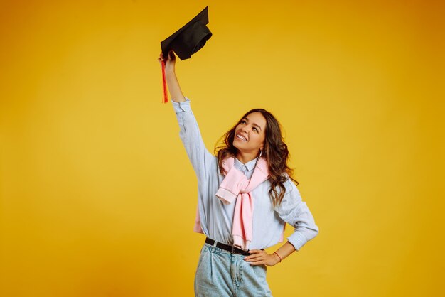 Retrato de mulher com um chapéu de formatura na cabeça dela posando em amarelo.