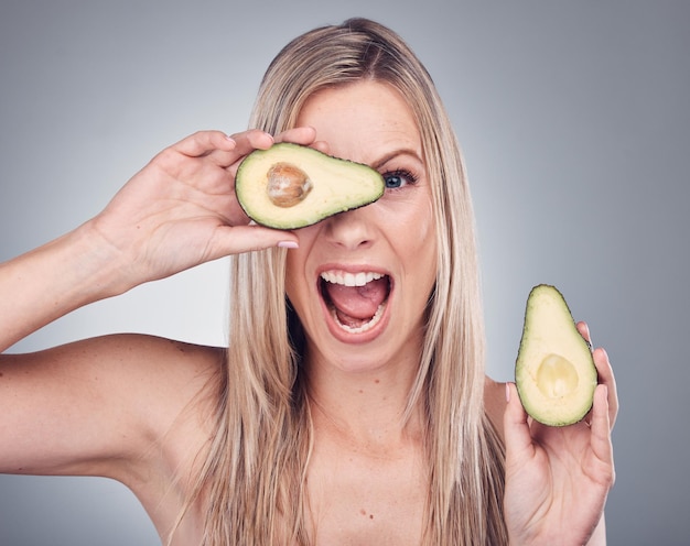 Retrato de mulher de cuidados com a pele e abacate de beleza em estúdio com brilho natural e brilho cosmético Rosto cômico de modelo estético animado em fundo cinza para benefícios sustentáveis de alimentos ou produtos para o cabelo