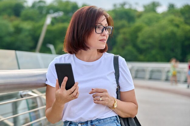 Retrato de mulher de meia idade andando com smartphone na mão dia de verão na cidade