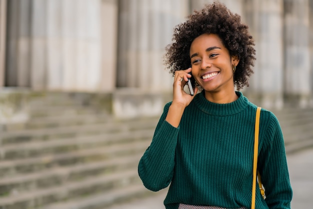 Foto retrato de mulher de negócios afro falando ao telefone em pé ao ar livre na rua