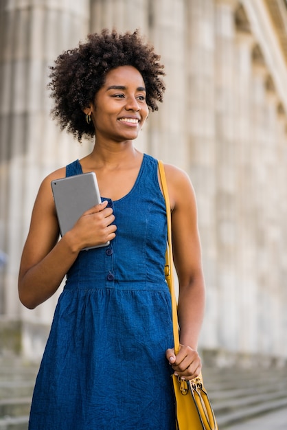 Retrato de mulher de negócios afro segurando um tablet digital em pé ao ar livre na rua. negócios e conceito urbano.