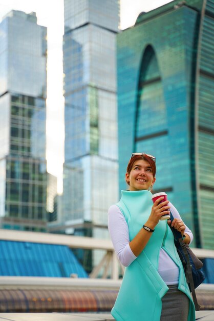 Retrato de mulher de negócios andando e sorrindo ao ar livre e xícara de café