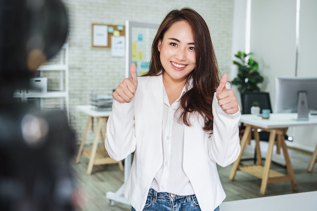 Retrato de mulher de negócios asiática com polegar para cima, como ao gravar um vídeo