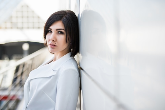 Retrato de mulher de negócios em um escritório moderno. Mulher de negócios confiante com os braços cruzados em pé encostado na parede de vidro.