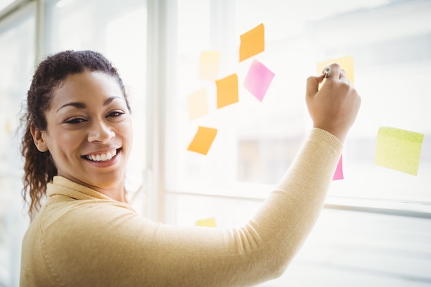 Retrato de mulher de negócios feliz escrevendo notas adesivas no escritório