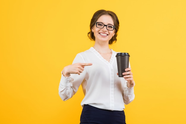 Retrato de mulher de negócios feliz sorridente jovem bonita confiante mostrando na xícara de café com a mão em amarelo