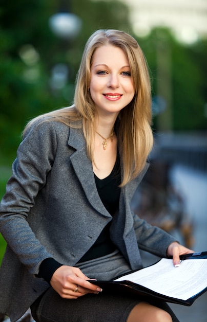 Retrato de mulher de negócios jovem sentado no banco com documentos