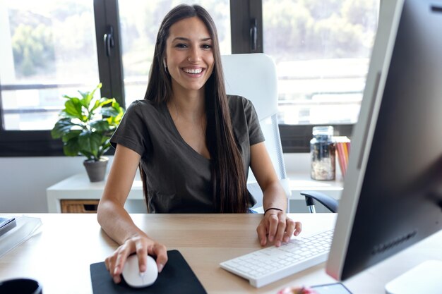 Retrato de mulher de negócios jovem sorridente, olhando para a câmera enquanto trabalhava com o computador no escritório.