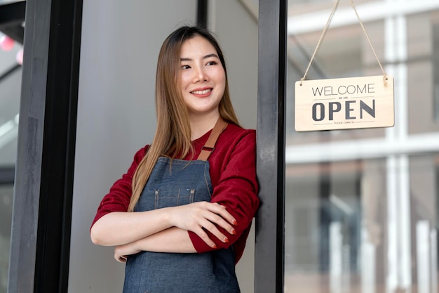 Retrato de mulher de negócios positiva em pé na entrada da porta do refeitório Alegre jovem garçonete no avental azul perto da porta de vidro com tabuleta aberta