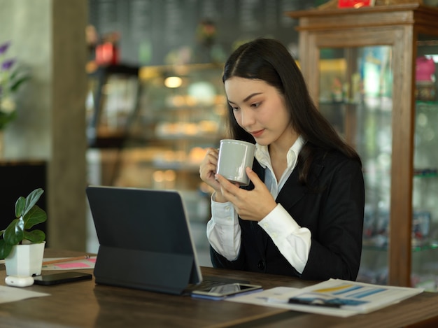 Retrato de mulher de negócios tomando café enquanto trabalha com um tablet e a papelada no café