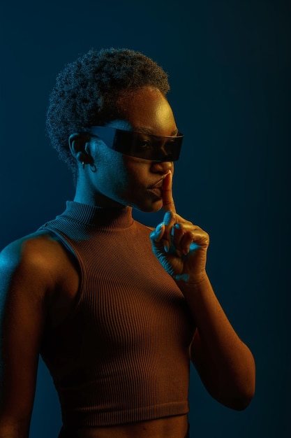 Retrato de mulher de óculos com gesto de silêncio sobre fundo de estúdio escuro e luz neon