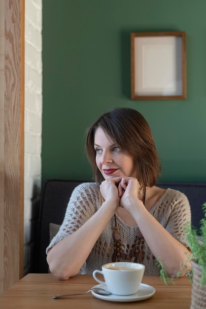 Retrato de mulher de trinta anos no café com café cappuccino latte mulher pensativa senta-se à mesa no café e olha pela janela