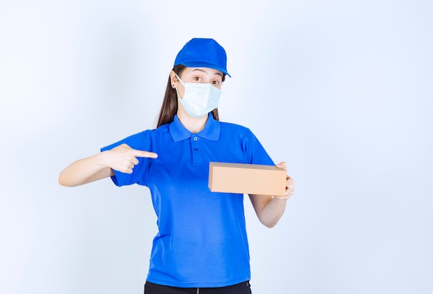 Retrato de mulher de uniforme e máscara médica apontando para a caixa de papel