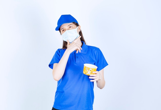 Retrato de mulher de uniforme e máscara médica segurando um copo de plástico