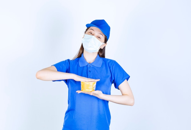 Retrato de mulher de uniforme e máscara médica segurando um copo de plástico