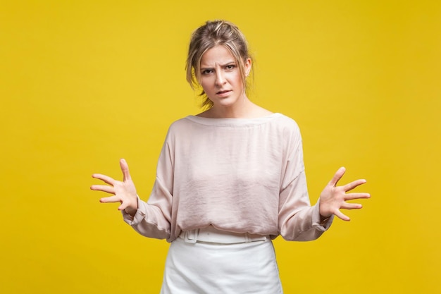 Retrato de mulher decepcionada irritada com cabelo loiro na blusa casual em pé com os braços levantados frustrado e com raiva enquanto discutia tiro de estúdio interior isolado em fundo amarelo