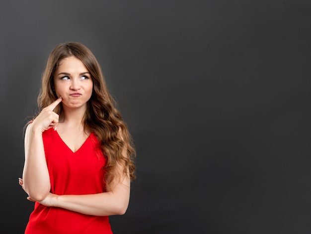 Retrato de mulher duvidosa. Antecedentes comerciais. Senhora confusa no pensamento vermelho isolado no espaço cinza da cópia.