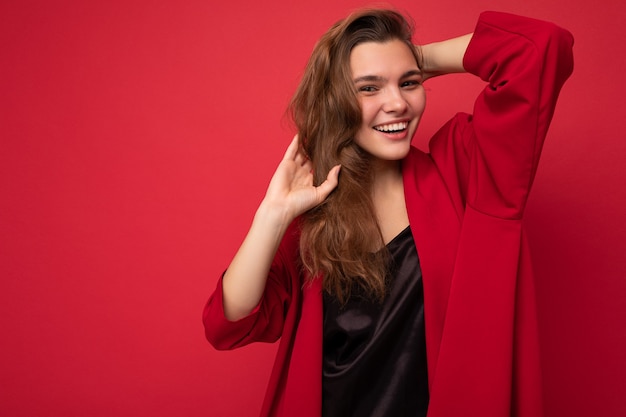 Retrato de mulher elegante alegre positiva em trajes formais, olhando para a câmera isolada no vermelho