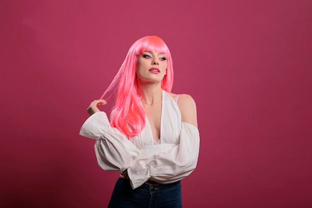 Retrato de mulher elegante usando peruca de cabelo rosa em estúdio, se divertindo com maquiagem elegante e penteado olhar na frente da câmera. Sentindo-se confiante, bonita e despreocupada com glamour moderno.